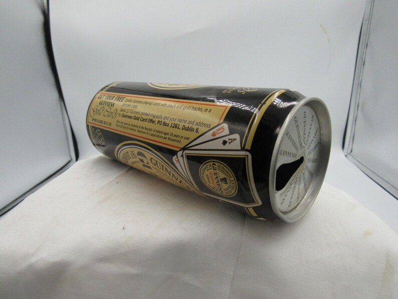 May include: A black Guinness beer can with gold accents and text. The can features a playing card design and the Guinness logo. The can is lying on its side, with the top partially visible.