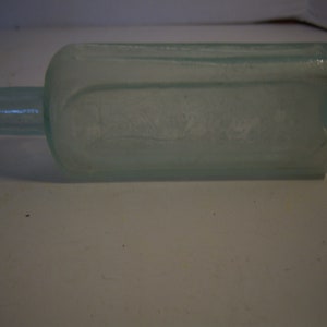 May include: A clear glass bottle with a rectangular body and a rounded neck. The bottle is frosted and has a slight green tint.