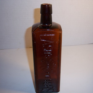 May include: A dark brown glass bottle with a square shape and a narrow neck. The bottle has embossed text that reads "Dr. J.H. McLean's Liver and Kidney Balm" and a graphic of a horse's head.