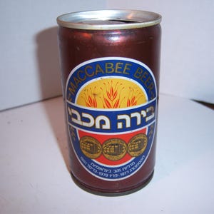 May include: A brown aluminum can with a blue and yellow label. The label says "Maccabee Beer" in English and "בירה מקבי" in Hebrew.