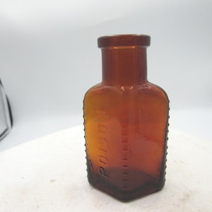 May include: Amber-colored antique poison bottle with the word "POISON" embossed vertically. The bottle has a square base and a rounded neck. The edges of the bottle are textured with small, raised dots.