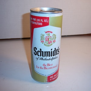 May include: A gold and red aluminum can of Schmidt's beer. The can has a crest with a lion and the text "Schmidts of Philadelphia" and "the Beer for the Bicentennial".
