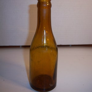May include: A brown glass bottle with a rounded bottom and a narrow neck. The bottle is empty and has a slightly frosted appearance.