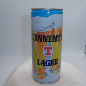 May include: A cylindrical Tennent's Lager beer can. The can features a blue top, a white and yellow body with the brand name and logo, and an image of beer glasses. The word "LAGER" is printed in large letters.