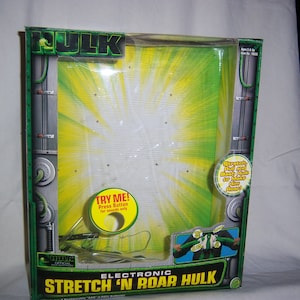 May include: Electronic "Stretch 'N Roar Hulk" toy packaging. The box is green and black with the word "Hulk" in green block letters. The packaging includes the text "Try Me! Press Button for sounds only."