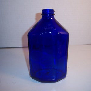 May include: A cobalt blue glass bottle with a wide mouth and a rounded bottom. The bottle is empty and has a slightly textured surface.