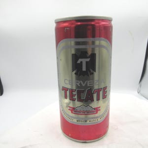 May include: A red and silver Tecate beer can. The can features the word "Tecate" in red, with a silver background and a black "T" logo. The can is cylindrical and appears to be full.