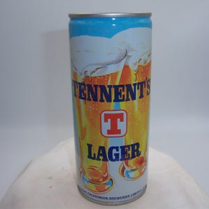 May include: A cylindrical Tennent's Lager beer can. The can features a blue top, a silver rim, and a white and orange design with the brand name and logo. The word "LAGER" is printed in large letters.