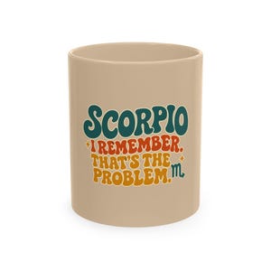 May include: A beige ceramic mug featuring the text SCORPIO I REMEMBER. THAT'S THE PROBLEM. in a retro-style font with teal, orange, and yellow colors. The design includes small star accents and the Scorpio zodiac symbol in teal on the right side.