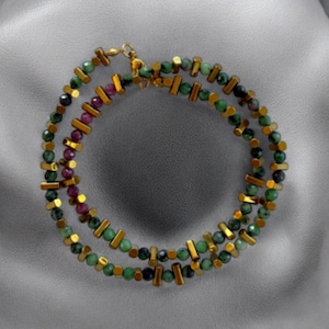 May include: A double-strand necklace featuring alternating round green and magenta beads interspersed with small, cylindrical gold-toned metal spacers. The necklace is secured with a gold-toned metal lobster claw clasp at the top.