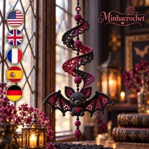 May include: A hanging crochet ornament featuring a dark gray bat with a red heart on its chest, suspended from a spiral structure of black and magenta lace-like crochet. The design includes small black beads and magenta spheres.
