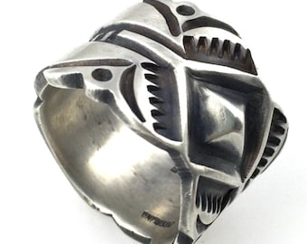 May include: A silver ring with an intricate geometric design. The ring features a series of angular shapes, including squares and triangles, with a textured surface. The ring is likely made of sterling silver and is a statement piece of jewelry.