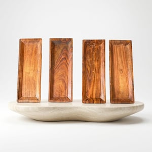 Puede incluir: Cuatro bandejas rectangulares de madera con un acabado de veta natural en tonos marrones. Cada bandeja presenta un centro poco profundo y bordes ligeramente elevados, dispuestas verticalmente para mostrar los patrones de la madera.