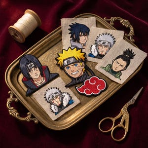 May include: A collection of embroidered fabric patches featuring anime characters and a red cloud symbol. The patches are displayed on a rectangular brass tray alongside a wooden spool of thread and gold-colored metal scissors with ornate handles.