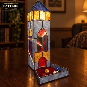 May include: A stained glass dice tower featuring a tall, multi-colored structure with blue, yellow, and red panels. The tower has a pointed roof and an open base with a red velvet tray containing several multi-sided gaming dice.