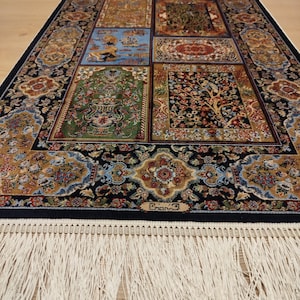 May include: A rectangular area rug featuring a dark blue border with intricate floral patterns and a central panel divided into four distinct sections with detailed illustrations of trees, animals, and foliage, finished with long white fringe.
