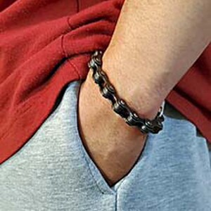 Puede incluir: Un brazalete de cadena de metal negro. El brazalete est&aacute; hecho de piezas de metal enlazadas que se asemejan a una cadena de bicicleta.