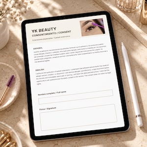 May include: A digital tablet displaying a YK Beauty eyelash extension consent form in Spanish and English. The screen shows text, a photo of an eye with a purple spoolie, and fields for a full name and signature. A white stylus rests beside the tablet.