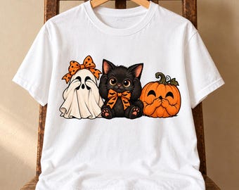May include: A white short-sleeved t-shirt featuring a graphic print of a ghost wearing an orange polka-dot bow, a black kitten with an orange bat-patterned bow, and a smiling orange pumpkin, all positioned side-by-side on the front.
