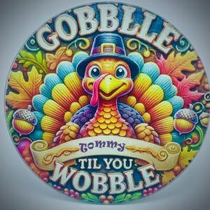 May include: A circular sign featuring a colorful cartoon turkey wearing a pilgrim hat, surrounded by autumn leaves and acorns. The text reads GOBBLE TIL YOU WOBBLE in bold lettering, with the word tommy centered on a scroll banner.