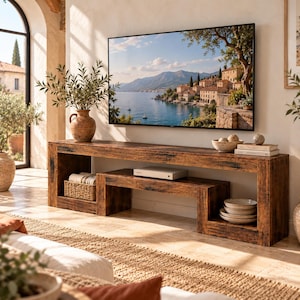May include: A long, dark brown wooden media console with a rectangular frame and a nested lower shelf. The console holds a woven basket, a white electronic device, and a stack of ceramic bowls. A large flat-screen television is mounted above.