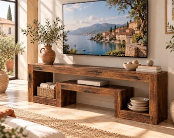 May include: A long, dark brown wooden media console with a rectangular frame and a nested lower shelf. The console holds a woven basket, a white electronic device, and a stack of ceramic bowls. A large flat-screen television is mounted above.