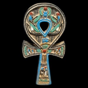 May include: An Egyptian ankh symbol featuring intricate carvings and painted details in blue, red, green, and white. The surface displays figures, a scarab beetle, and hieroglyphic motifs across the circular top and the vertical crossbar.