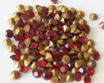 May include: A large pile of red and gold rhinestones. The rhinestones are scattered on a white surface.