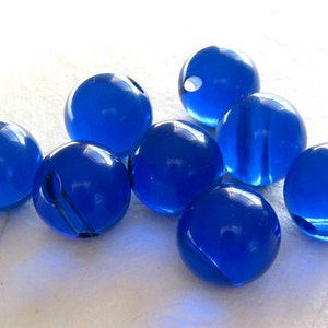 May include: A group of eight blue glass beads. The beads are round and have a smooth, shiny finish.