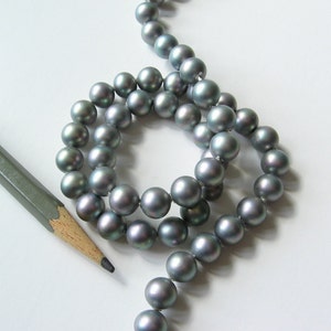 May include: A strand of gray pearls, arranged in a circle, with a pencil lying on a white surface.