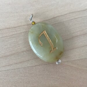 May include: A light green oval pendant with a gold letter 'I' inscribed on it. The pendant is attached to a silver chain.