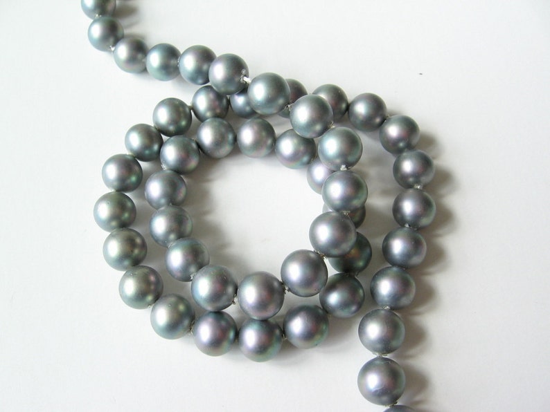 May include: A strand of gray pearls with iridescent shimmer. The pearls are strung on a thin thread and are arranged in a circular pattern.