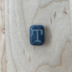 May include: A dark blue stone with the letter "T" carved into it in white.