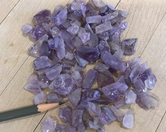 May include: A large pile of small, purple amethyst crystal chips on a wooden surface.