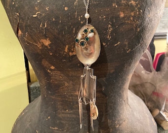 May include: A silver spoon necklace with a cluster of green and white rhinestones. The spoon is attached to a silver chain and has a long, dangling design.