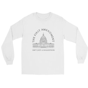 May include: A white long-sleeve shirt featuring a black line-art illustration of the United States Capitol building. The text "THE FIRST AMENDMENT" is arched above the building, and "ISN'T JUST A SUGGESTION" is printed in black below it.