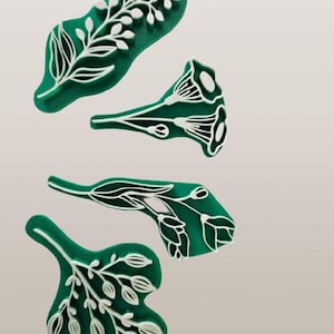 May include: Four green stamps with white raised designs of various botanical elements including leafy branches, trumpet-shaped flowers, and small buds. Each stamp features a distinct floral pattern with clean lines and a flat base for printing.