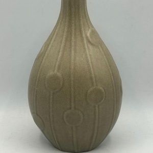 May include: A teardrop-shaped ceramic vase in a muted taupe color. The surface features a textured pattern of vertical lines intersected by raised circular motifs that wrap around the body, leading up to a narrow, cylindrical neck opening.