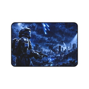Puede incluir: Una alfombrilla de escritorio rectangular con una ilustración monocromática en azul oscuro de un soldado futurista con armadura que sostiene un rifle. La escena muestra un horizonte urbano en ruinas bajo la lluvia y un cielo tormentoso con luces.