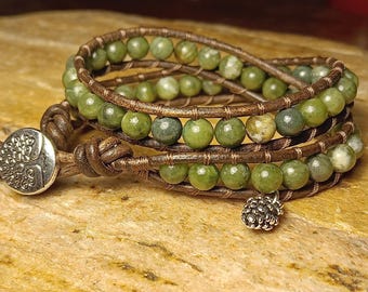 May include: Wrap bracelet with green jade beads and brown leather. The bracelet has a silver button clasp and a small silver charm. The beads are a mix of green shades. This wrap bracelet is a stylish accessory.