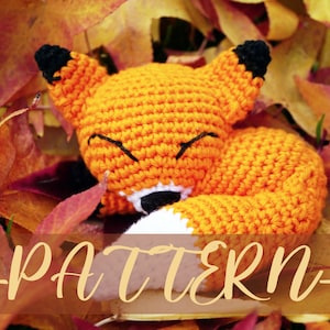 Puede incluir: Un zorro naranja de crochet con ojos negros y una cola de punta blanca, acostado sobre una cama de hojas de otoño. El texto "PATTERN" está escrito en marrón en la parte inferior de la imagen. El texto "Miss Bjo Collection" está escrito en negro en la esquina superior derecha de la imagen.