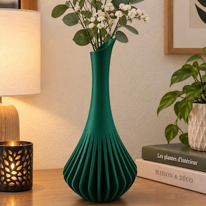 May include: A tall, dark green vase with a slender neck and a wide, pleated base. The vase features a matte finish and vertical ridges that extend from the bottom to the middle section, holding a bouquet of white flowers and green eucalyptus leaves.