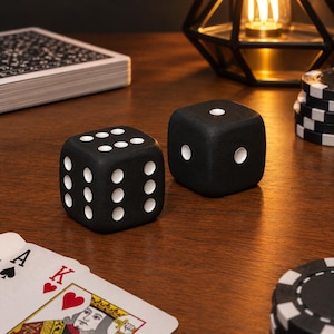 Peut inclure: Deux dés noirs mats avec des points blancs, l'un affichant un six et l'autre un deux, placés près d'un jeu de cartes et d'une pile de jetons de poker noirs et blancs sur une surface en bois sous un éclairage chaleureux.