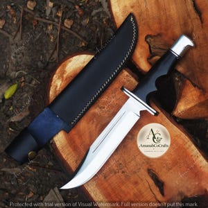 Puede incluir: Un cuchillo de hoja fija con una hoja de acero plateado pulido, un mango negro y un pomo plateado. El cuchillo viene acompañado de una funda de cuero negro con costuras blancas. Se observa un logotipo circular con el texto AmanahCoCrafts.