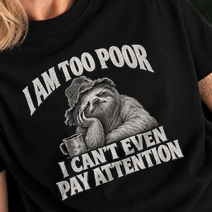 Könnte beinhalten: Ein schwarzes T-Shirt mit einer Grafik eines Faultiers mit Hut, das seinen Kopf neben einer Tasse auf eine Hand stützt. Der Text über dem Faultier lautet I AM TOO POOR und der Text darunter lautet I CAN'T EVEN PAY ATTENTION in weißer Schrift.