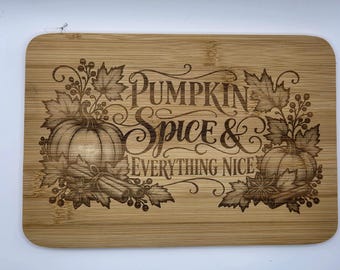 Puede incluir: Una tabla de cortar rectangular de bambú con un diseño grabado a láser de calabazas, hojas de arce, ramas de canela y anís estrellado. El texto PUMPKIN SPICE & EVERYTHING NICE aparece en una combinación de letra cursiva y serif.