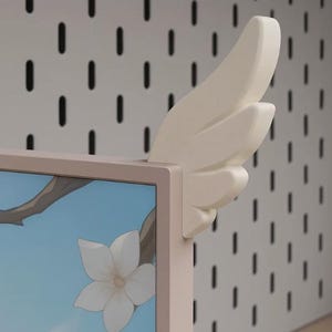 May include: A cream-coloured, wing-shaped decorative attachment mounted on the top corner of a rectangular frame. The frame displays a light blue screen with a graphic of a white flower on a brown branch, featuring a smooth, matte finish.