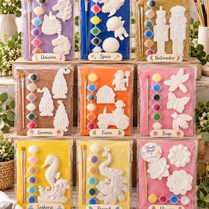 May include: Nine craft kits in clear plastic packaging, each containing white plaster figures, paint pots, and brushes. Themes include unicorn, space, nutcracker, gnomes, farm, bugs, seahorse, peacock, and flowers, with labels identifying each set.