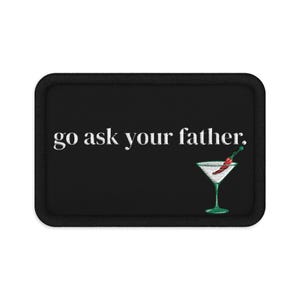 May include: A rectangular black embroidered patch with a thick black border. The text "go ask your father." is stitched in white letters. Below the text is an embroidered martini glass containing a red chili pepper on a green cocktail pick.