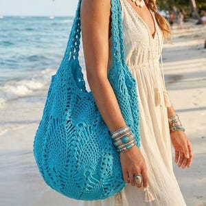 May include: A bright turquoise crochet shoulder bag featuring an intricate openwork pattern, a wide strap, and a spacious, slouchy silhouette. The bag is crafted from yarn with a textured, knotted design, showcasing a detailed geometric motif.